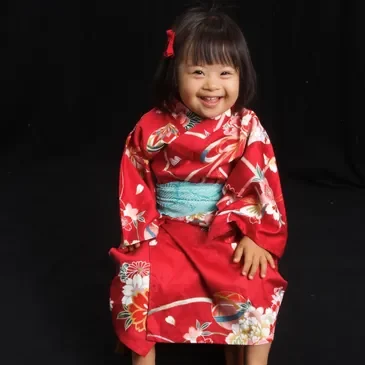 A little girl in a red kimono sitting on the ground.